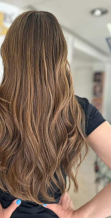 Cabello largo castaño con baby lights cálidos, de espalda